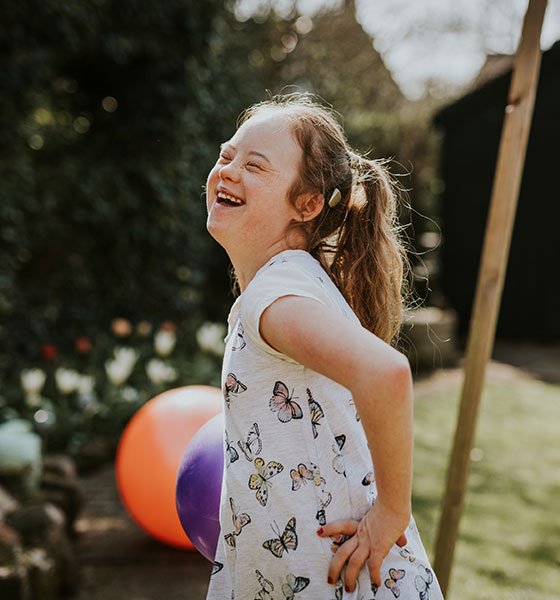 Lachendes Mädchen mit Down-Syndrom spielt im Garten – Symbol für Vertrauen und liebevolle Vertretung in der Verhinderungspflege